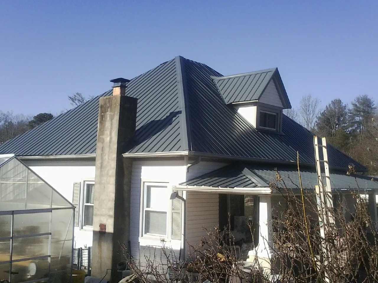 Dark blue standing seam metal roof on a white farmhouse with dormer — Slate & Tile Roof Repair by Roofing Brothers in Crandon