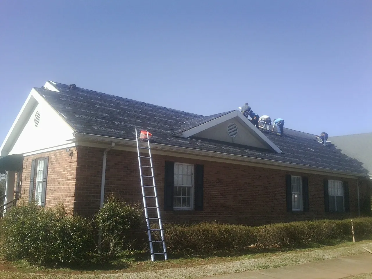 Crew tearing shingles off a brick ranch roof with a ladder set — Emergency Roof Repair work by our crew in Crandon