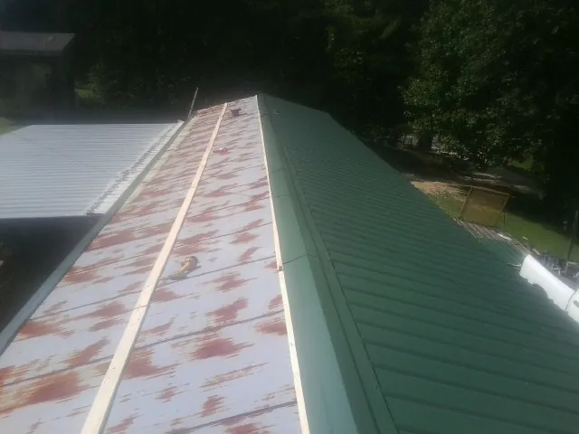 Old rusted panels beside newly installed green metal roofing — Wind Damage Roof Repair by Roofing Brothers in Crandon