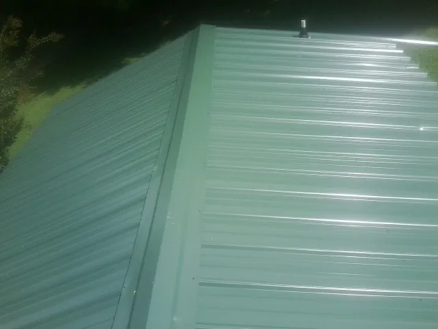New green metal panels meeting at the ridge of a roof — Flat Roof Repair work by our crew in Crandon