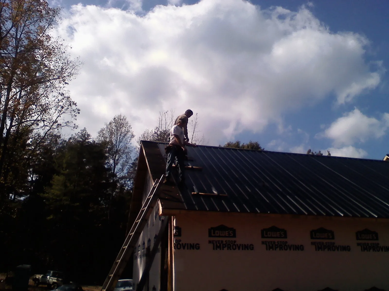 Roofer fastening dark metal panels high against a cloudy sky, from a Roof Inspection job in Crandon