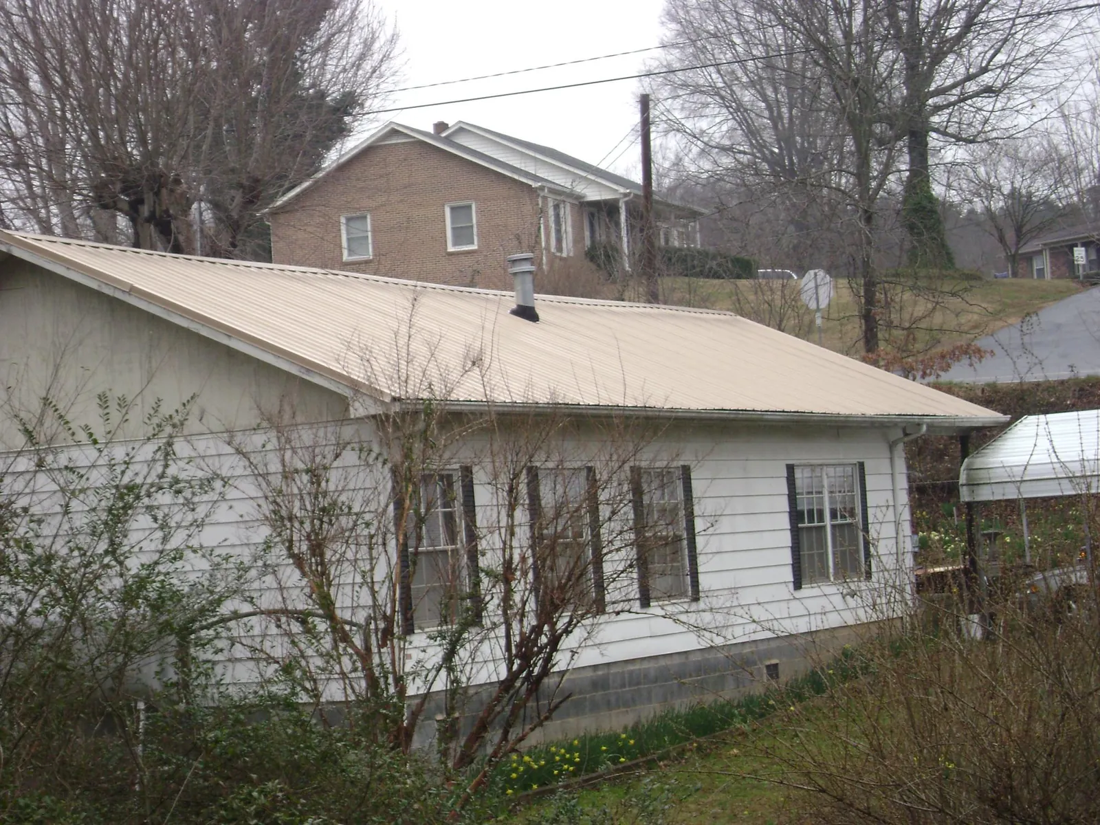 Tan metal roof on a white sided house set into a hillside — Commercial Roofing by Roofing Brothers in Crandon