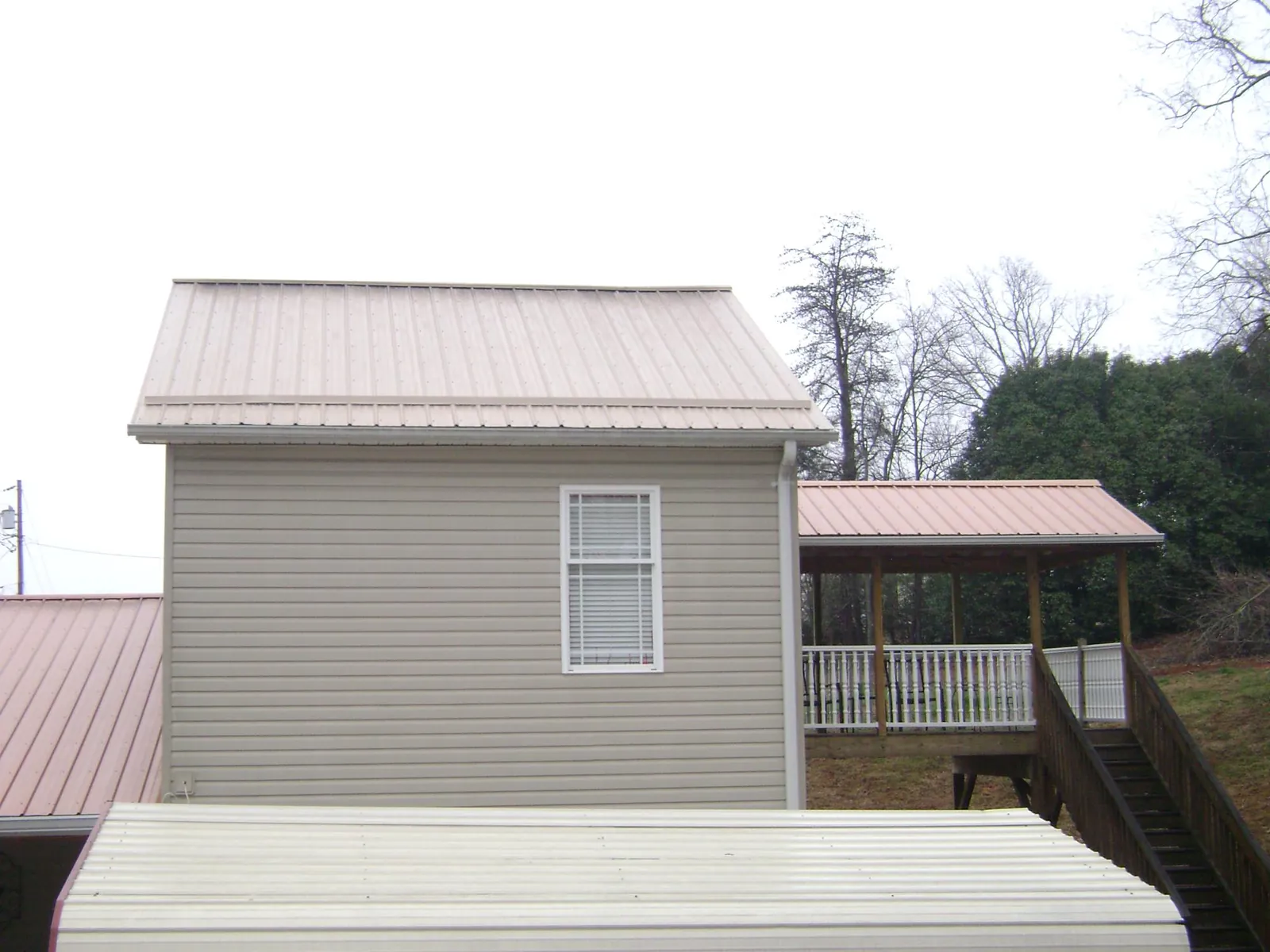 Tan metal roofs on a two story addition and attached porch, from a Roof Replacement job in Crandon